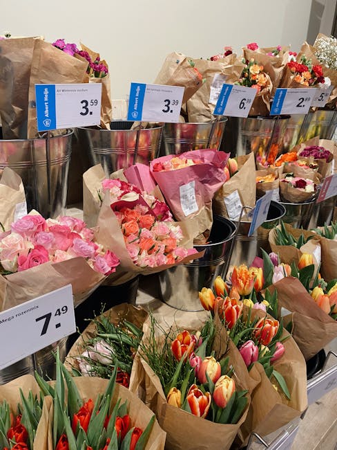 An assortment of fresh floral bouquets arranged in metal containers and paper wraps at a flower shop, priced between £2.50 and £7.49. The bouquets include vibrant pink roses, orange and pink tulips,